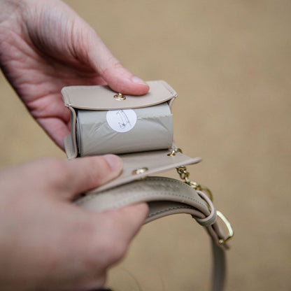 Beige handbag with a small round mirror inside, held by a person against a beige background.